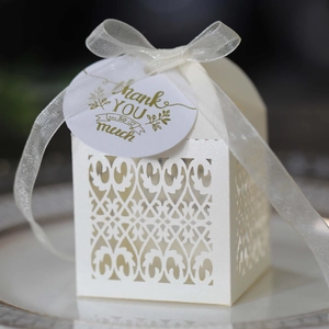 Close-up of laser-cut wedding favor box with white ribbon and golden thank you tag