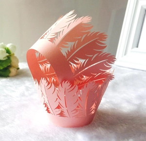 Macro detail of laser-cut pink paper cupcake wrapper featuring intricate feather patterns