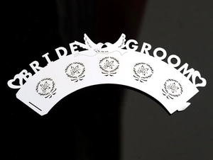 Macro detail of laser-cut Bride and Groom white cupcake wrapper with bird wreath