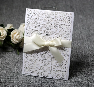 Detailed laser-cut floral wedding invitation with a cream satin bow on grey texture