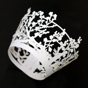 Detail of laser-cut floral pattern cupcake wrappers in white paper on black background