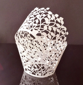 Macro shot of laser-cut leaf pattern on white cupcake wrappers for wedding dessert decor