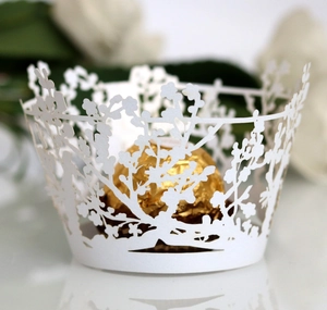 Detail of laser-cut white cupcake wrapper with tree and floral pattern for weddings