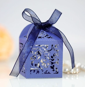 Detail of purple laser-cut wedding candy box with intricate floral pattern and blue ribbon