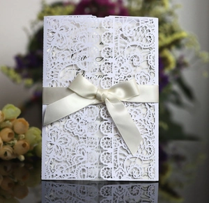 Detailed laser-cut white lace wedding invitation with an elegant beige satin bow
