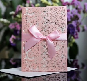 Detailed laser-cut lace invitation card with elegant pink satin ribbon and floral accents