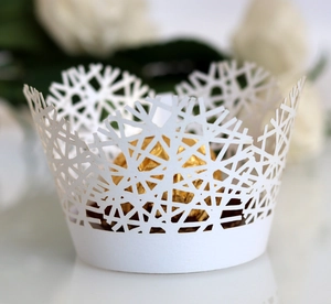 Close-up of laser-cut white cupcake wrapper with intricate snowflake patterns for weddings