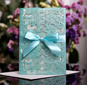 Detailed close-up of teal laser-cut lace wedding invitation with a satin ribbon bow