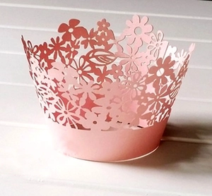 Detailed laser-cut flower patterns on light pink cupcake wrappers for wedding decor