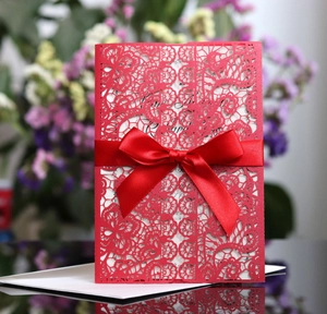 Close-up of laser-cut red wedding invitation with silk bow and white inner paper insert