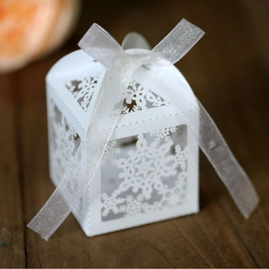 White laser-cut snowflake gift box with silk ribbon on a rustic wooden background