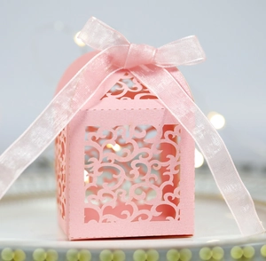 Elegant laser-cut pink wedding favor box with ribbon on decorative white tray