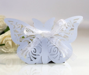 Close-up of laser-cut butterfly wedding favor box with white organza ribbon and floral decor