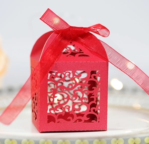Detail of red laser-cut wedding candy box with elegant scroll pattern and silk ribbon bow