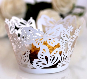Close-up of white laser-cut cupcake wrapper with butterfly and floral hollow design