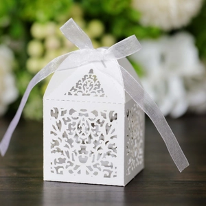 Elegant white laser-cut wedding favor box with intricate vine patterns and silk ribbon bow