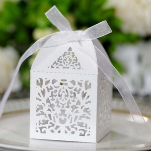 Detailed laser-cut pattern on white wedding favor box with ribbon on a ceramic plate