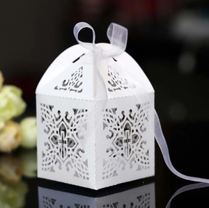 Macro shot of white laser-cut wedding favor box with intricate patterns and satin ribbon
