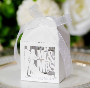 Macro shot of white laser-cut Mr & Mrs wedding candy box with a white ribbon bow on a plate