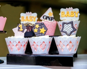 Macro view of laser-cut muffin wrappers with decorative Baby One cake toppers