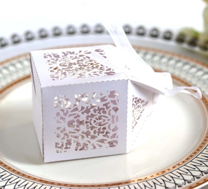 Close-up of white laser-cut floral wedding favor box with a silk ribbon on a plate