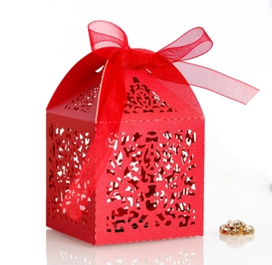 Macro detail of red laser-cut wedding favor box with intricate patterns and silk ribbon