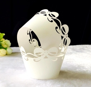 Detailed laser-cut white cupcake wrapper featuring elegant bow patterns and intricate textures