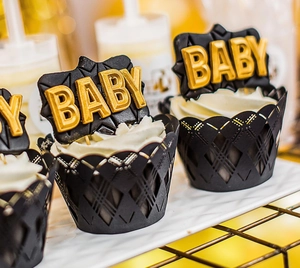 Close-up of black laser-cut lace cupcake wrapper and gold BABY topper for baby shower