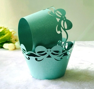 Detail of mint green laser-cut cupcake wrapper with pearl glitter finish and bow pattern