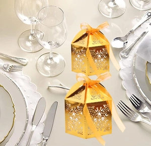Detail view of laser-cut gold wedding favor boxes with elegant orange ribbons on a table