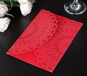 Detail of red laser-cut wedding invitation with intricate floral patterns on wood