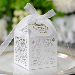 Close-up of white laser-cut wedding favor box with ribbon and thank you tag on a plate