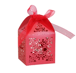 Detail of red laser-cut wedding favor box with intricate hollow pattern and silk ribbon
