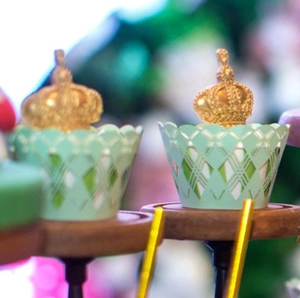 Detail of mint green geometric cupcake wrappers and gold crown toppers in outdoor setting