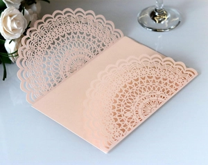 Detail of laser-cut lace pattern on pearlescent paper wedding invitation in soft pink