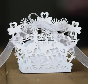 Detail of white laser-cut hollow candy box with bird and heart patterns and organza ribbon