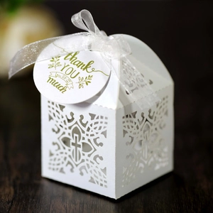 Detail of laser-cut cross pattern on white wedding favor box with ribbon and thank you tag