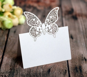 Laser-cut white butterfly place cards with heart hollow design on vintage wood table
