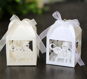 Detail of laser-cut elephant candy boxes with sheer organza ribbons on wood surface