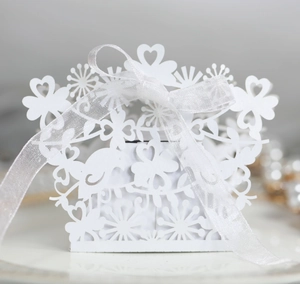 Detail of white laser-cut wedding favor box with hollow bird and floral heart patterns