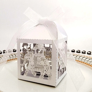 Detailed laser-cut elephant hollow favor box with white organza ribbon bow on a plate
