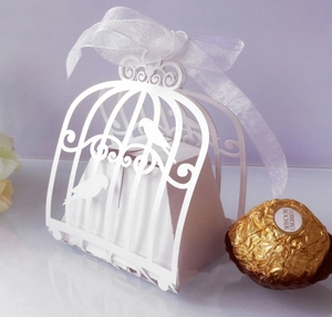 Detail of laser-cut birdcage candy box with intricate white floral pattern and silk bow
