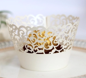 Close-up of laser-cut white lace cupcake wrapper with intricate floral scroll patterns