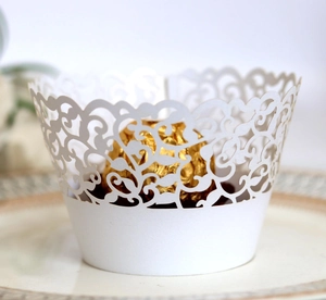 Close-up of white laser-cut lace cupcake wrapper with elegant floral vine patterns