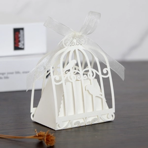 Detail of white laser-cut birdcage candy box with ribbon bow on a rustic wood background