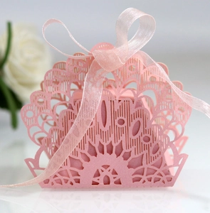 Detail of pink laser-cut wedding favor box with peacock lace pattern and ribbon bow