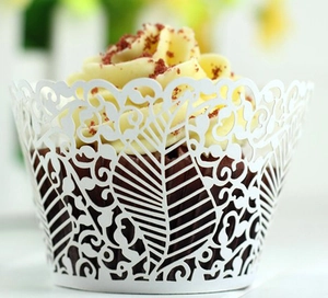 Close-up of white laser-cut cupcake wrapper with intricate leaf vine and lace patterns