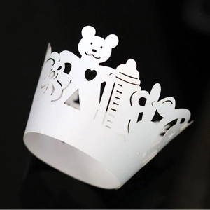 White laser-cut cupcake wrappers with bear and bottle patterns for baby shower decor