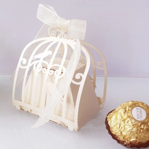 Close-up of white laser-cut birdcage candy box with elegant ribbon and hollow pattern