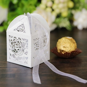 Detailed laser-cut white rose favor box with elegant organza ribbon on dark wood surface